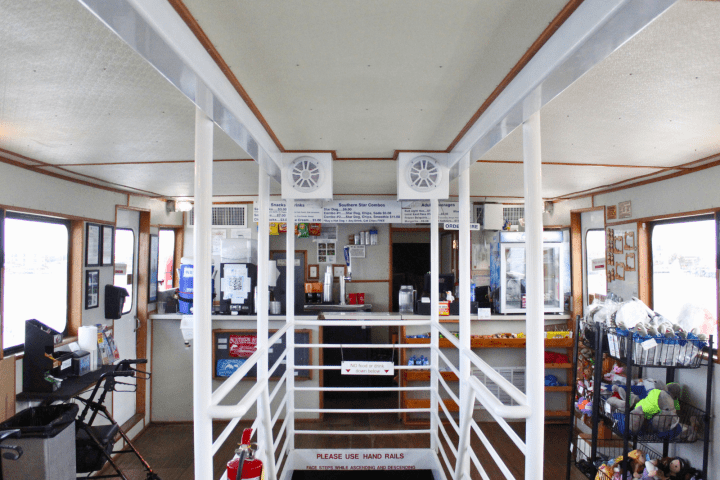 Interior of a ferry with a snack bar, seating areas, and safety equipment like extinguishers and handrails.