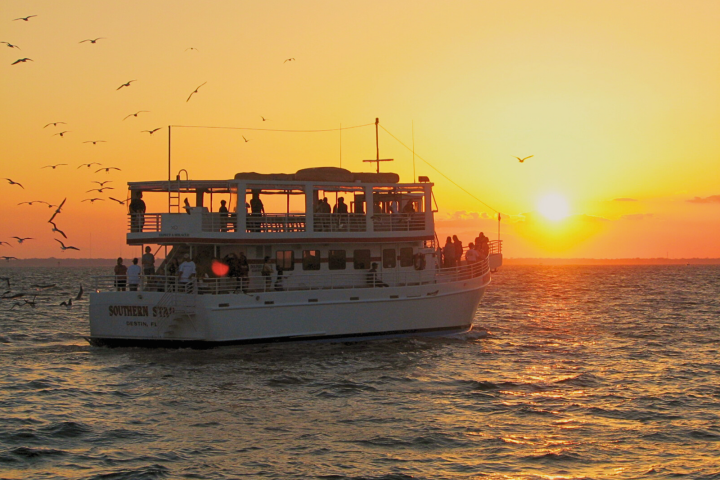Boat on water at sunset with seagulls flying above.