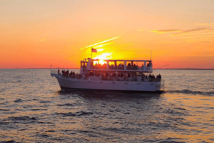 Boat on water at sunset with orange and yellow sky, and American flag visible on top.