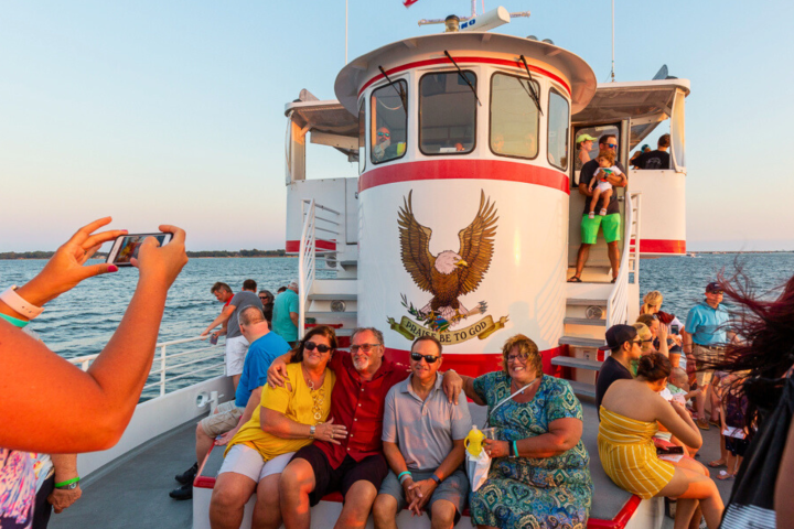 People on a boat deck with an American flag and eagle emblem at sunset.