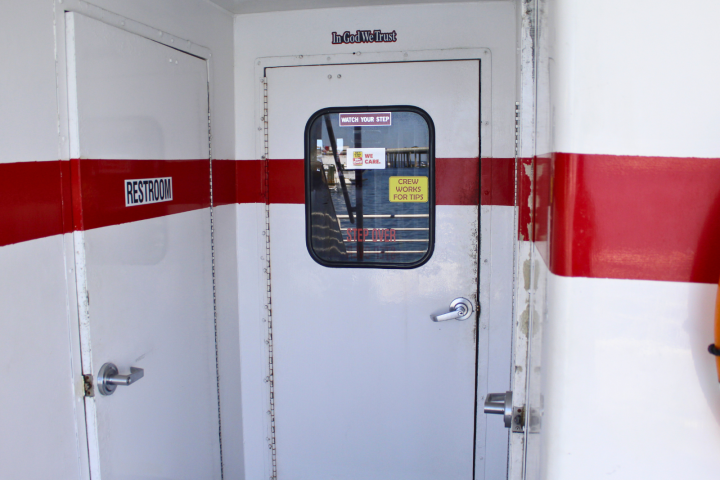 Ship door with red stripe, restroom sign, and window displaying caution stickers.