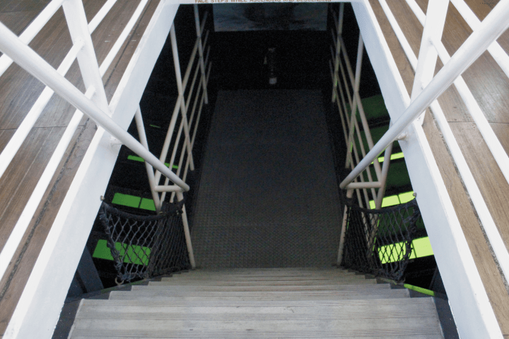 Stairwell with white handrails and warning sign above steps, leading down to lower level.
