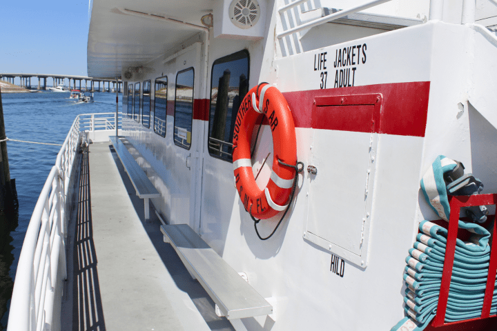 Side view of a docked boat with a red life preserver and benches, bridge visible in the background.