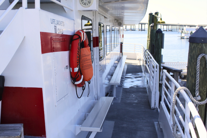 Boat deck with life jackets mounted on the side, overlooking a calm harbor.