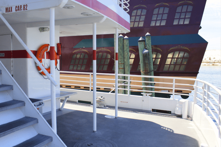 Deck of a ferry with a pirate ship in the background on a sunny day.