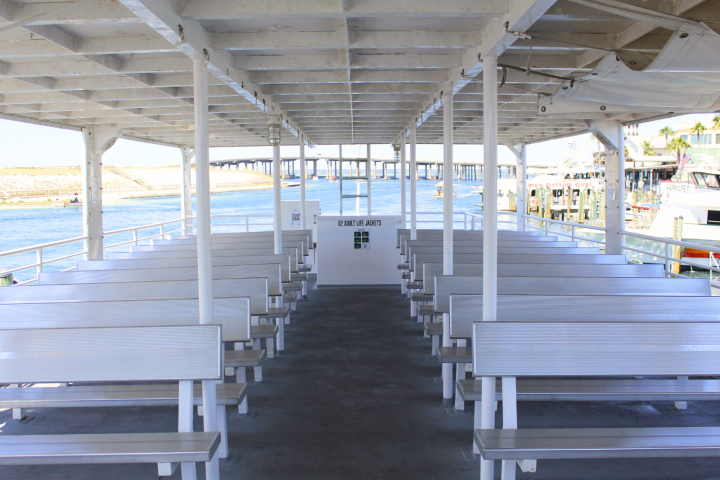 Empty ferry deck with rows of benches and view of water and docks.