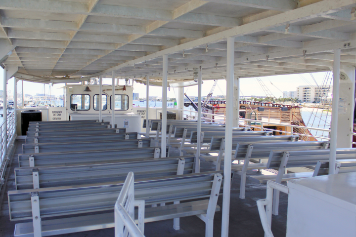 Empty passenger ferry deck with rows of metal benches and view of a docked ship.