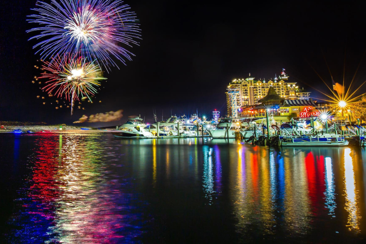 Colorful fireworks over a marina with brightly lit boats at night.