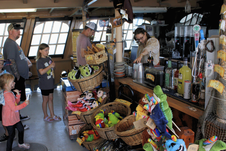 People at a gift shop counter with plush toys and drinks, children browsing.