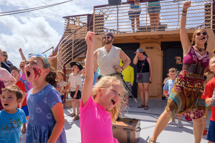 Children and adults excitedly participating in a pirate-themed event on a ship deck.