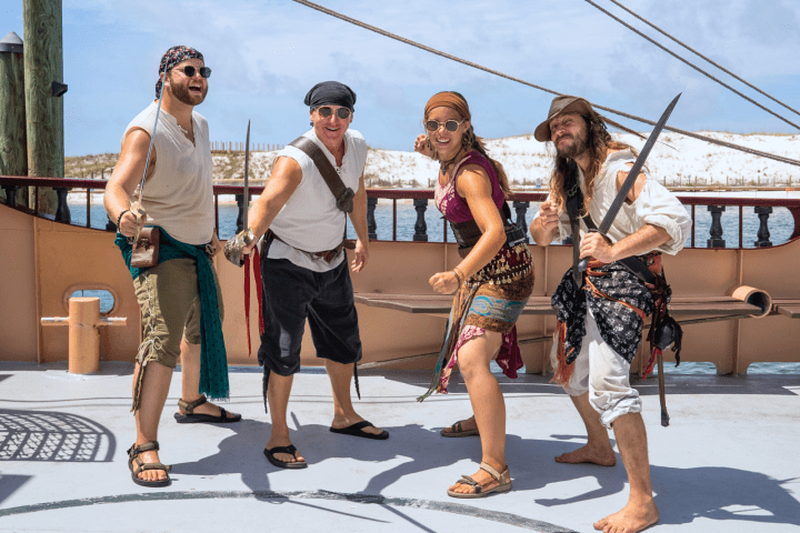 Four people dressed as pirates posing on a ship deck with swords drawn.