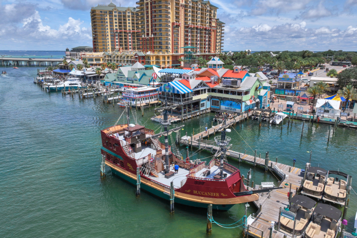 Aerial view of a coastal harbor with a pirate-themed ship and colorful buildings along the shoreline.