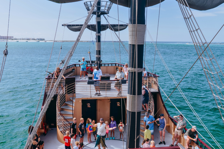 People on a sailboat deck enjoying the ocean view on a sunny day.
