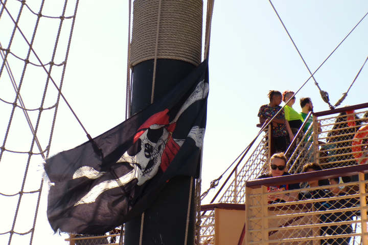 Pirate flag with skull and crossbones on ship's mast, people on deck.